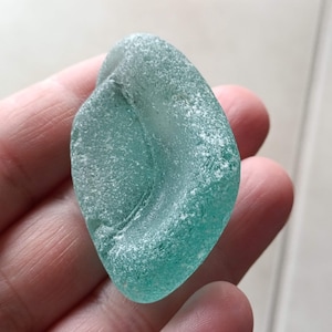 Puede incluir: Una pieza de vidrio de mar liso, azul claro, con un acabado esmerilado. El vidrio tiene una forma curva única.