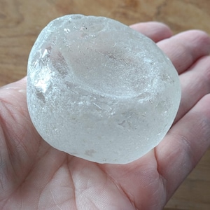 Puede incluir: Una pieza de vidrio de mar liso, blanco y redondo, con forma de cuenco. El vidrio tiene una superficie esmerilada y texturizada.