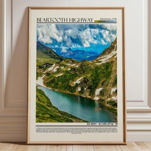 May include: Framed print of Beartooth Highway in Montana, USA. The landscape features a turquoise lake, green hills, and snow-capped mountains under a cloudy sky. The print includes the highway name and coordinates.