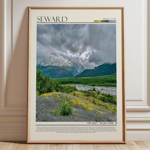 May include: Framed print featuring a scenic view of Seward, Alaska, USA. The image showcases a dramatic sky over lush green mountains and a riverbed. The word "Seward" is printed at the top, with coordinates at the bottom. The overall color palette includes greens, grays, and browns.