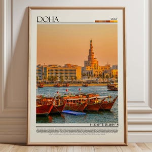 Puede incluir: Un póster enmarcado de Doha, Qatar. La imagen muestra una escena frente al mar con barcos de madera tradicionales, edificios modernos y una estructura alta en forma de espiral. La palabra "DOHA" está en la parte superior, con coordenadas en la parte inferior.