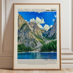 Könnte beinhalten: Gerahmter Druck mit einer Landschaft der Dolomiten in den italienischen Alpen. Das Bild zeigt einen blauen See, grüne Bäume und hohe Berggipfel unter einem blauen Himmel mit weißen Wolken. Der Druck enthält den Text "Dolomites Mountains" und geografische Koordinaten.