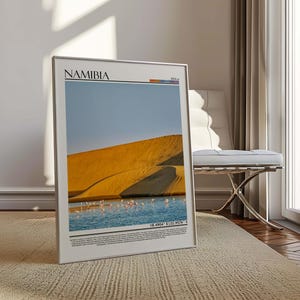 May include: A framed print featuring a landscape of Namibia. The image shows a golden sand dune, a body of water with pink flamingos, and a blue sky. The word "NAMIBIA" is printed at the top of the frame.