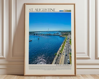 May include: A framed print featuring an aerial view of St. Augustine, Florida, with the city's name at the top. The image shows a bridge over blue water, boats, and a road with cars. The sky is clear blue.