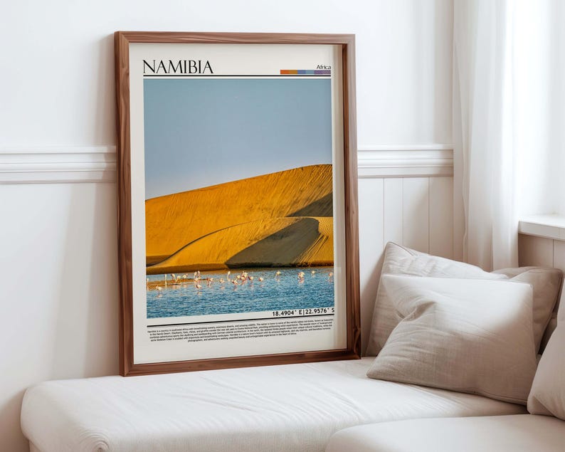 May include: Framed print featuring a scenic view of Namibia. The image showcases a golden sand dune, a body of water with pink flamingos, and a clear blue sky. The word "NAMIBIA" is printed at the top, with coordinates at the bottom.