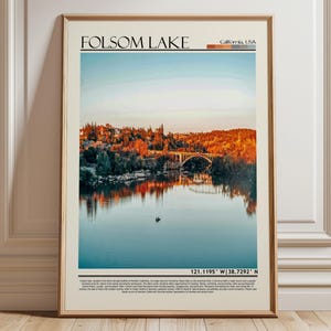 May include: Framed poster featuring Folsom Lake in California, USA. The image showcases a serene lake scene with a bridge and trees reflecting in the water. The poster includes the text "Folsom Lake" and coordinates.