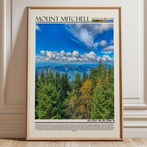 May include: Framed print featuring a scenic view of Mount Mitchell in North Carolina, USA. The image showcases a vibrant blue sky with fluffy white clouds, lush green trees, and distant mountain ranges. The text "Mount Mitchell" is at the top.