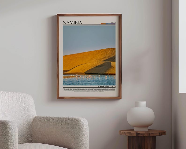 May include: A framed print featuring a Namibian landscape with a golden sand dune, blue water, and a flock of birds. The print has the word "NAMIBIA" at the top and coordinates at the bottom. The frame is made of wood.