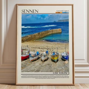 May include: Framed print featuring a coastal scene in Sennen, Cornwall, England. The image showcases colorful fishing boats on a concrete surface, with a stone wall and ocean in the background. The print includes the text "Sennen" and coordinates.