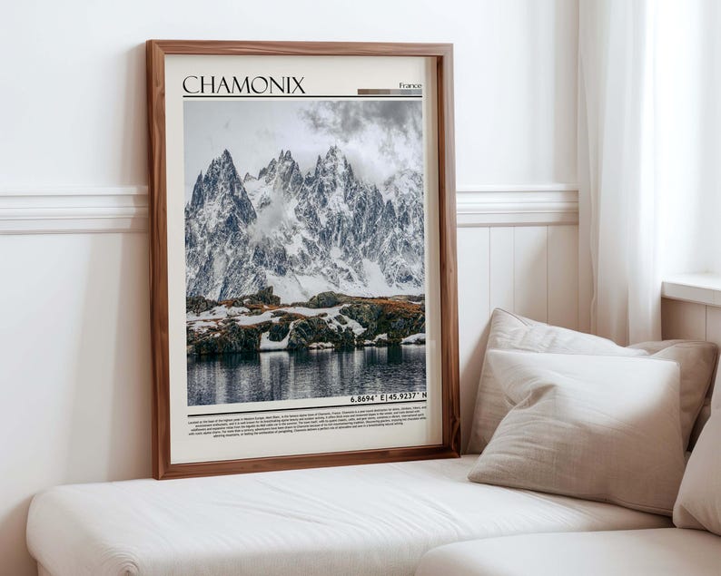 Może przedstawiać: Oprawiony wydruk przedstawiający krajobraz Chamonix, Francja. Obraz przedstawia ośnieżone g&oacute;ry odbijające się w jeziorze pod zachmurzonym niebem. Wydruk ma napis "CHAMONIX" u g&oacute;ry i wsp&oacute;łrzędne na dole, wszystko w drewnianej ramie.