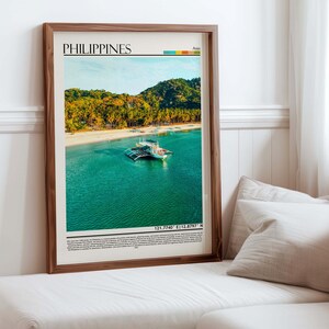 May include: A framed print featuring a vibrant photograph of the Philippines. The image showcases a tropical beach with a boat on turquoise water, lush green hills, and the text "PHILIPPINES" at the top. The frame is a warm brown color.