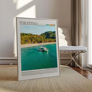 May include: A framed print featuring a tropical beach scene in the Philippines. The image shows a boat in turquoise water, a sandy beach, and lush green hills under a blue sky. The word "PHILIPPINES" is at the top.