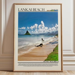 May include: A vertical wall art print in a light wood frame featuring a photograph of Lankai Beach, Hawaii, USA. The image shows a sandy beach, turquoise water, a distant island, and blue sky with clouds. Text includes the location and coordinates.