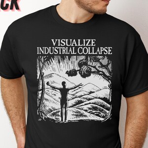 Peut inclure: T-shirt noir avec un motif blanc repr&eacute;sentant une personne debout dans un paysage montagneux, les bras tendus. Le texte "Visualize Industrial Collapse" est imprim&eacute; au-dessus du motif.