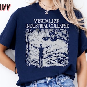 Peut inclure: Un t-shirt bleu marine avec un imprim&eacute; graphique blanc d'une personne debout dans un paysage de montagne. Le texte "Visualize Industrial Collapse" est imprim&eacute; au-dessus du graphique.