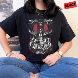 May include: Black t-shirt with a graphic print of a character from the anime Attack on Titan. The character is surrounded by other characters and the text "進撃の巨人" is printed below the graphic.