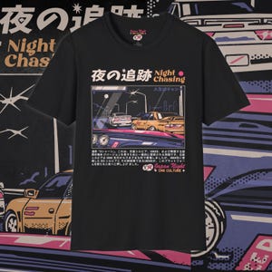 Könnte beinhalten: Schwarzes T-Shirt mit einem Grafikdruck von zwei Autos, die nachts fahren. Der Text "Night Chasing" ist in Pink und Weiß auf dem Shirt gedruckt. Der Text "Japan Night Car Culture" ist in Weiß am unteren Rand des Shirts gedruckt.