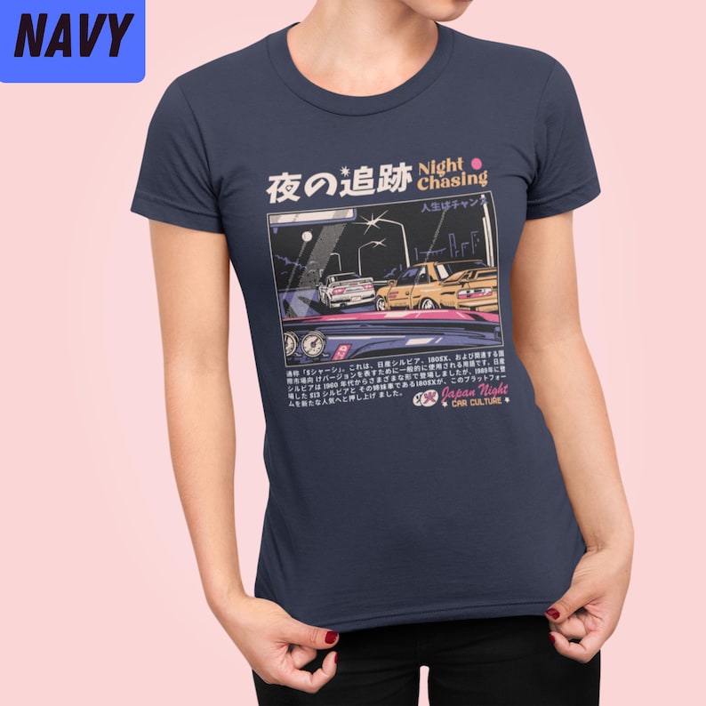 May include: A navy blue t-shirt with a graphic of two cars driving at night. The graphic is in a retro video game style. The text on the shirt reads "Night Chasing" and "Japan Night Car Culture".