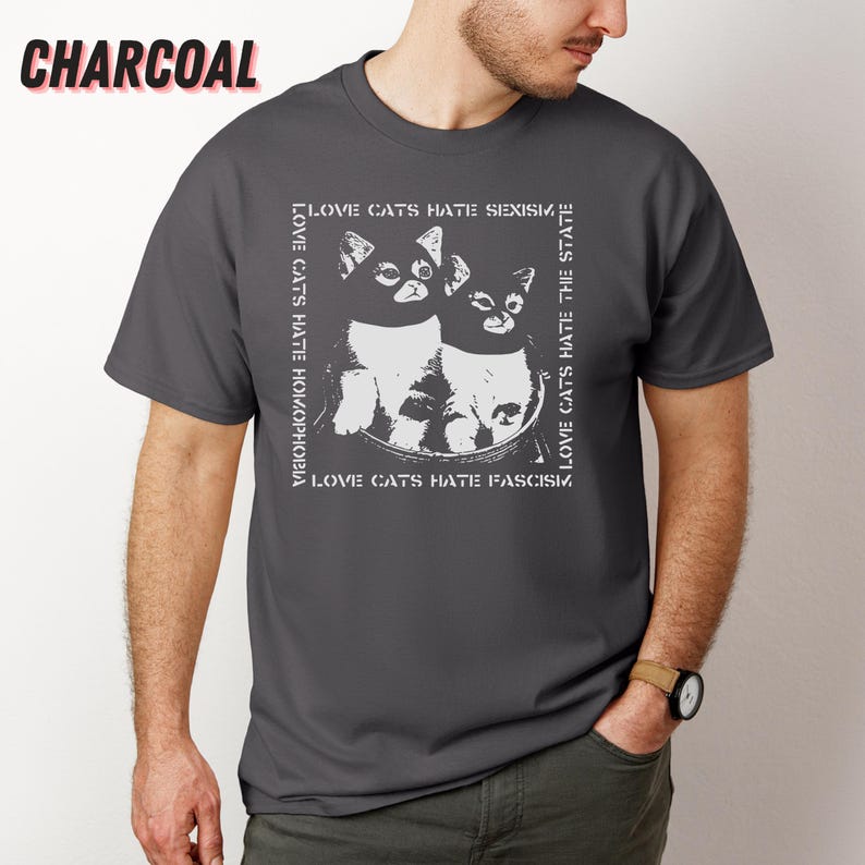 Op de afbeelding: Antracietgrijs t-shirt met een zwart-witte afbeelding van twee katten. De tekst rond de katten luidt "LOVE CATS HATE HOMOPHOBIA", "LOVE CATS HATE SEXISM", "LOVE CATS HATE THE STATE" en "LOVE CATS HATE FASCISM".