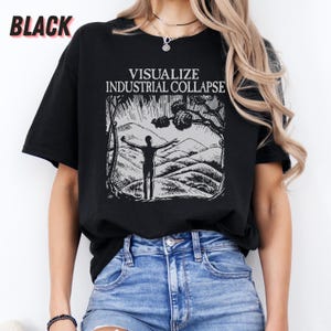 Peut inclure: Un t-shirt noir avec un imprim&eacute; graphique blanc d'une personne debout, les bras tendus devant une cha&icirc;ne de montagnes. Le texte "VISUALIZE INDUSTRIAL COLLAPSE" est imprim&eacute; au-dessus du graphique.