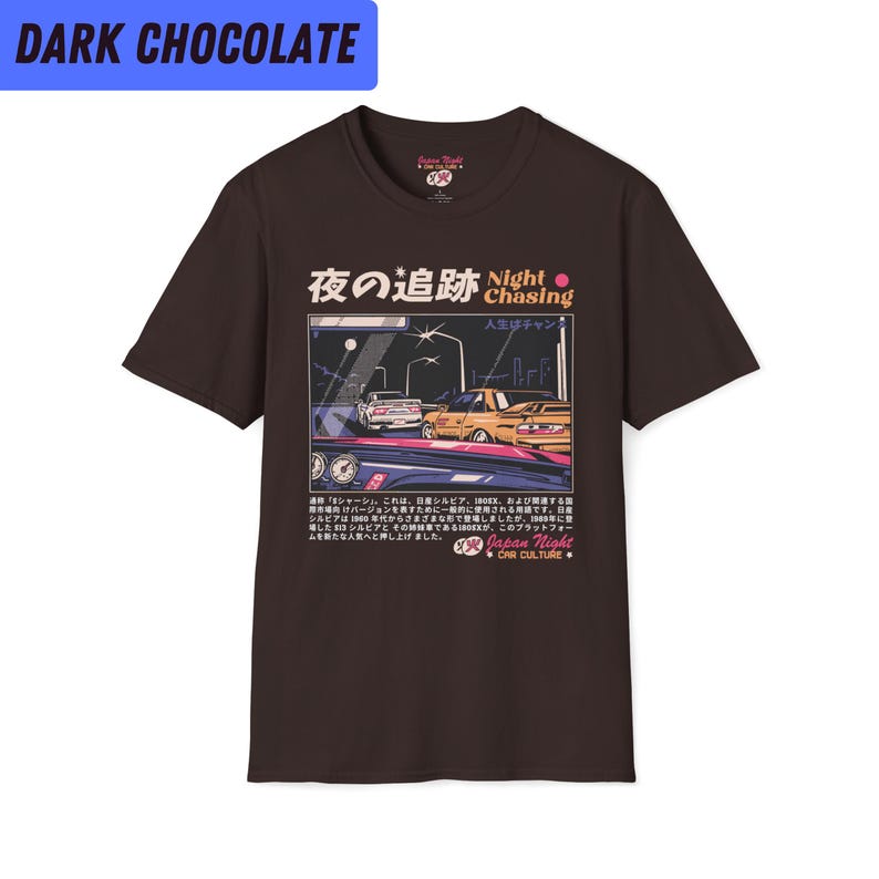 May include: A dark brown t-shirt with a graphic print of a night scene with cars driving on a road. The text "Night Chasing" is printed in pink and white on the shirt. The Japanese text "夜の追跡" is also printed on the shirt.