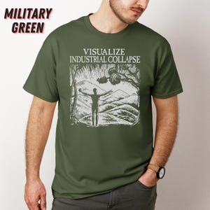 Peut inclure: Un t-shirt vert militaire avec un imprim&eacute; graphique blanc d'une personne les bras tendus devant un paysage de montagne. Le texte "Visualize Industrial Collapse" est imprim&eacute; au-dessus du graphique.