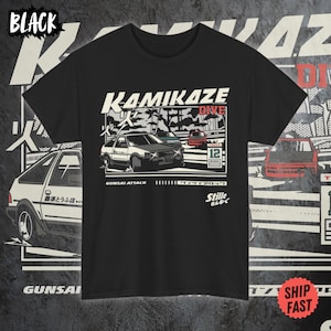 Può includere: Maglietta nera con una grafica bianca di un'auto da corsa con il testo "Kamikaze Dive" e "Gunsai Attack".