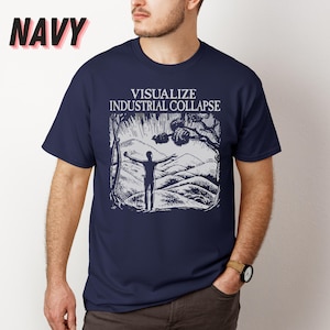 Peut inclure: Un t-shirt bleu marine avec un imprim&eacute; graphique blanc d'une personne debout, les bras tendus devant une cha&icirc;ne de montagnes. Le texte "VISUALIZE INDUSTRIAL COLLAPSE" est imprim&eacute; au-dessus du graphique.
