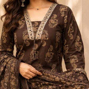 May include: A dark brown long-sleeved kurta featuring a gold floral block print pattern. The garment has a V-neckline with a decorative border and a matching brown fabric tassel. A coordinating brown and gold printed dupatta is draped over the arm.