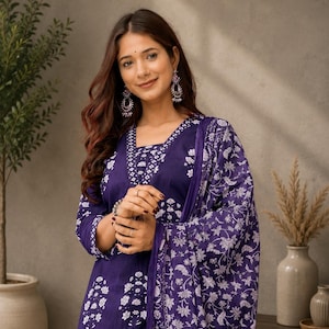 May include: A deep purple kurta set featuring a white floral block print pattern. The garment includes a square neckline with detailed white geometric trim along the edges and three-quarter length sleeves, paired with a matching printed dupatta.