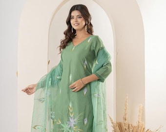 Puede incluir: Un conjunto de salwar kameez verde bordado. El atuendo incluye una túnica de manga larga, pantalones a juego y una dupatta transparente. La túnica y la dupatta presentan bordados florales en tonos verdes, blancos y morados. La modelo lleva el conjunto.