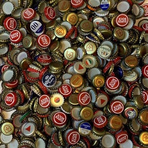 Könnte beinhalten: Nahaufnahme eines großen Haufens verschiedener Kronkorken. Viele sind rot und goldfarben, mit dem Text "SUPER BOCK" in Weiß. Andere Kapseln haben verschiedene Designs und Farben, darunter Weiß, Blau und Gelb. Die Kapseln sind verstreut und überlappen sich.