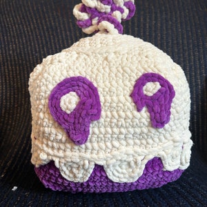 May include: A white crocheted ghost with purple eyes and a purple crocheted base. The ghost has a white and purple crocheted top.