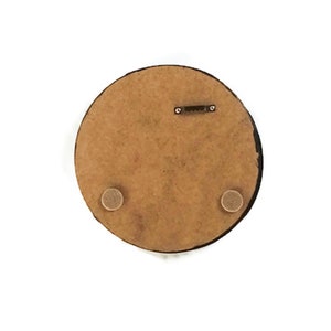 K&ouml;nnte beinhalten: Runde Wandkunst aus Holz, von hinten betrachtet. Die braune Oberfl&auml;che hat einen schwarzen Rand. Mit S&auml;gezahnaufh&auml;nger und zwei kleinen, kreisf&ouml;rmigen Pads zum Schutz der Wand.