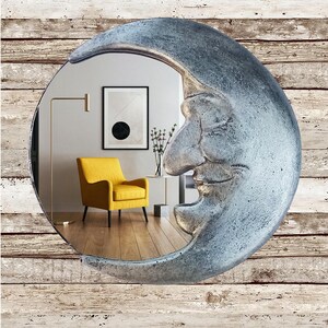 May include: A decorative wall mirror shaped like a crescent moon with a smiling face. The mirror has a silver finish and reflects a room with a yellow armchair, artwork, and a floor lamp. The background is a wood-plank wall.