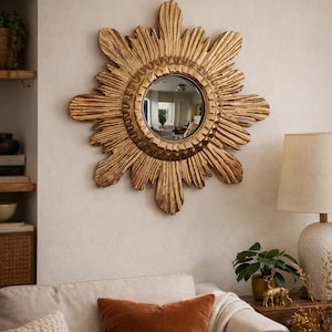 Puede incluir: Un espejo de pared circular con un marco de color dorado prominente diseñado con rayos de sol radiantes. El cristal central es redondo y reflectante, rodeado por un borde texturizado y tallado que imita la apariencia de rayos de sol estilizados.