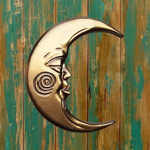 May include: A gold crescent moon wall decor with a face and a spiral design on a teal and brown wood background.