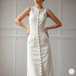 Puede incluir: Un vestido blanco sin mangas con cierre de botones en la parte delantera y dos bolsillos grandes. El vestido tiene un corpi&ntilde;o ajustado y una falda fluida.