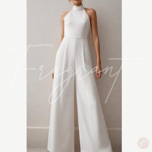 May include: A white halter jumpsuit with a high neck and wide legs. The jumpsuit is made of a smooth, flowing fabric.