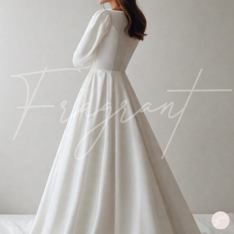 May include: A white, long-sleeved wedding dress with a V-neckline and a flowing skirt. The dress has a fitted bodice and a button detail down the back. The word "Fragrant" is written in cursive across the front of the dress.