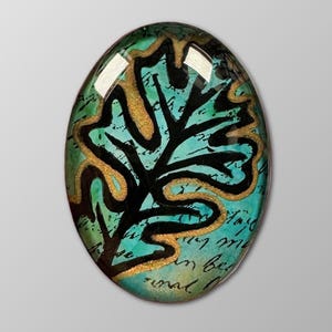 May include: Oval-shaped decorative glass piece with a leaf design. The leaf is black with gold outlines, set against a teal background with script writing. The edges are dark green.