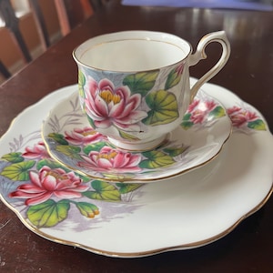 May include: A white teacup and saucer set with a pink and green floral design. The set features a delicate floral pattern with pink water lilies and green leaves.