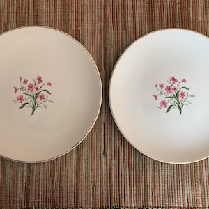 May include: Two white ceramic dinner plates with a gold rim and a pink floral design.