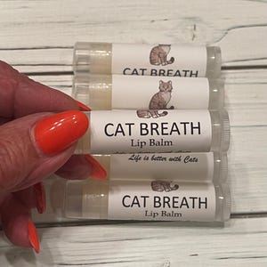 May include: Four clear lip balm tubes with white labels. The labels have a cartoon cat and the text "CAT BREATH Lip Balm" and "Life is better with Cats".