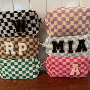 May include: A stack of six checkered cosmetic bags in various colors: black and white, brown and tan, green and white, pink and white, light blue and white, and purple and yellow. Each bag has a letter patch: W, RP, A, and MIA.