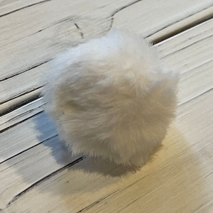 May include: A white fluffy pom pom, perfect for adding a touch of whimsy to crafts and projects.