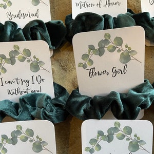 May include: Set of ten green velvet scrunchies with white cards featuring eucalyptus leaves and text. The cards read "Bridesmaid", "Matron of Honor", "Flower Girl", "I can't say I Do Without you!", "I do Crew", and "Bride Tribe".