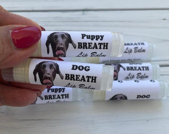May include: A set of four lip balms with dog-themed labels. The labels feature a black dog with the text "Puppy Breath Lip Balm", "Dog Breath Lip Balm", "Dog Breath Lip Balm", and "Dog".