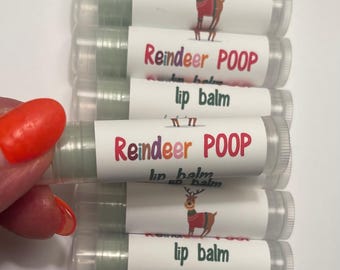 May include: A stack of lip balm tubes with white labels featuring a cartoon reindeer and the words "Reindeer POOP lip balm." The lip balm is a light green color, and the labels also say "herbal mint flavor."