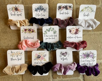 May include: Ten cards with floral designs and the words "bride tribe", "bride squad", "I Do Crew", "bride", "bridesmaid", "To have and to hold your love back", "Matron of honor", "Flower Girl", "Mom", "maid of honor", and "I can't say I Do without You!" Each card has a velvet scrunchie in a different color.